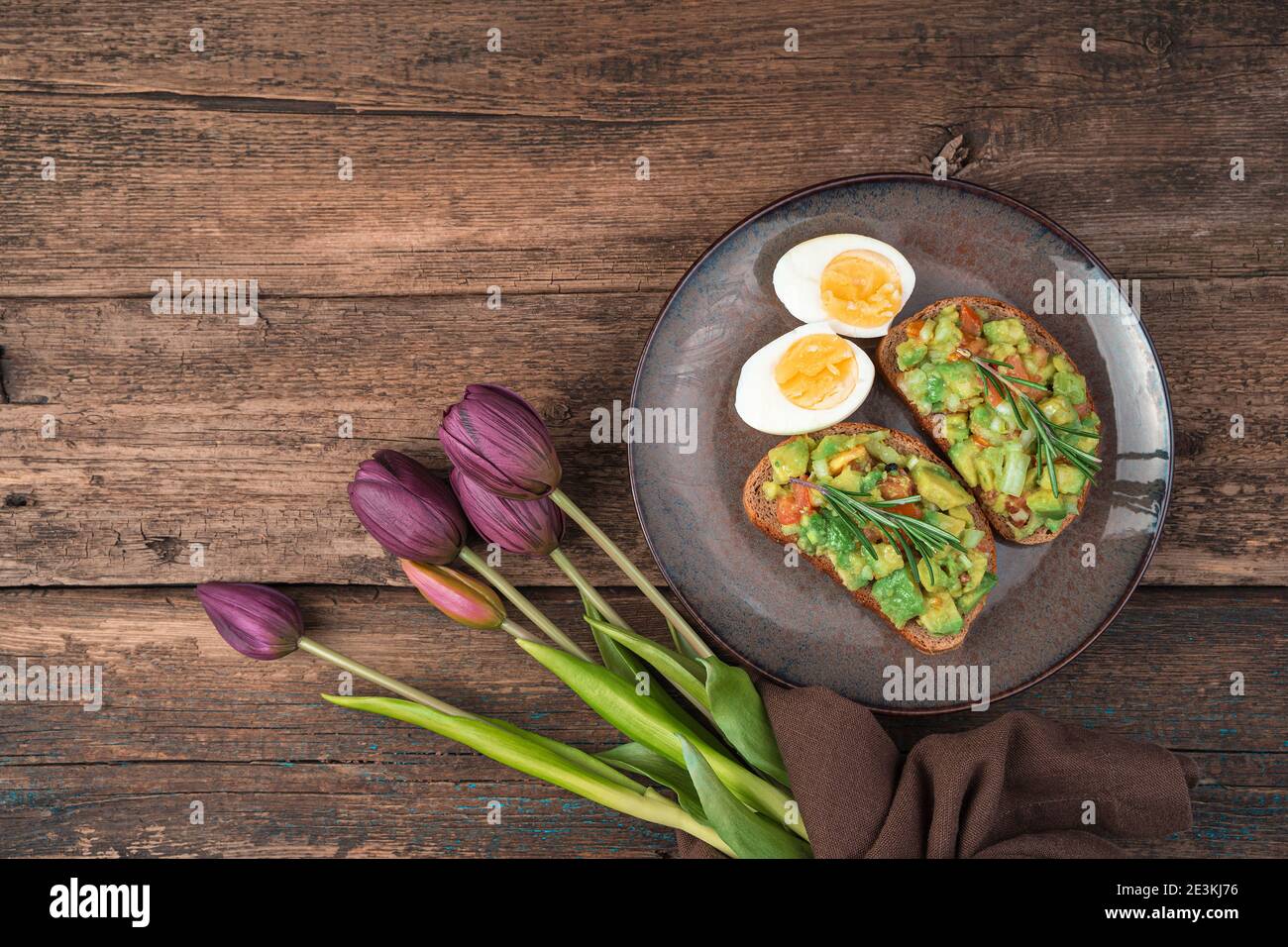 Toast à l'avocat, aux œufs et aux tulipes sur fond de bois. Banque D'Images