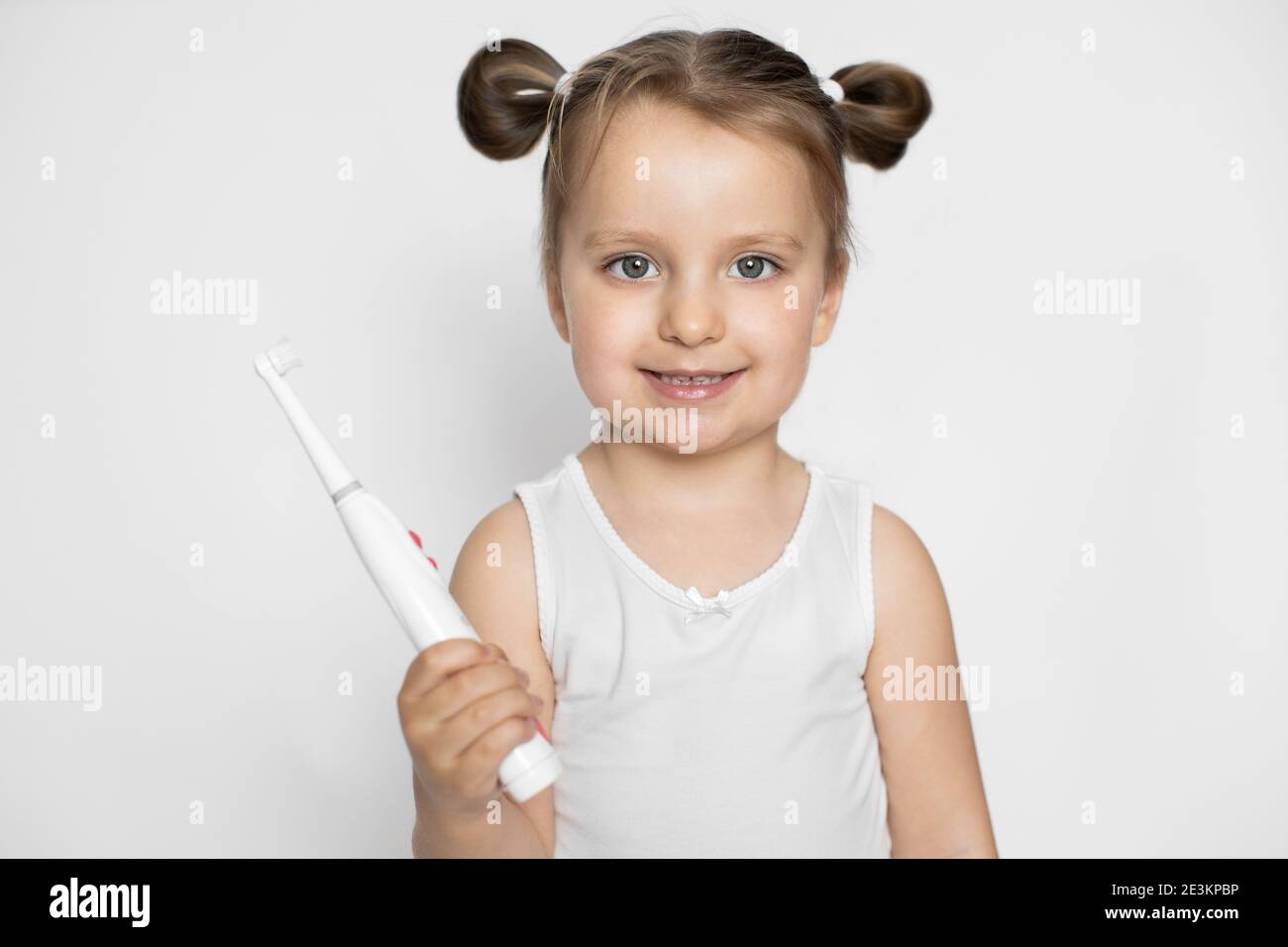 Petite Blonde 3 Ans Bebe Fille En Haut Blanc Et Deux Queues De Cheval Tenant La Brosse A Dents Electrique Souriant A L Appareil Photo Sur Un Fond Isole Dentaire Photo Stock