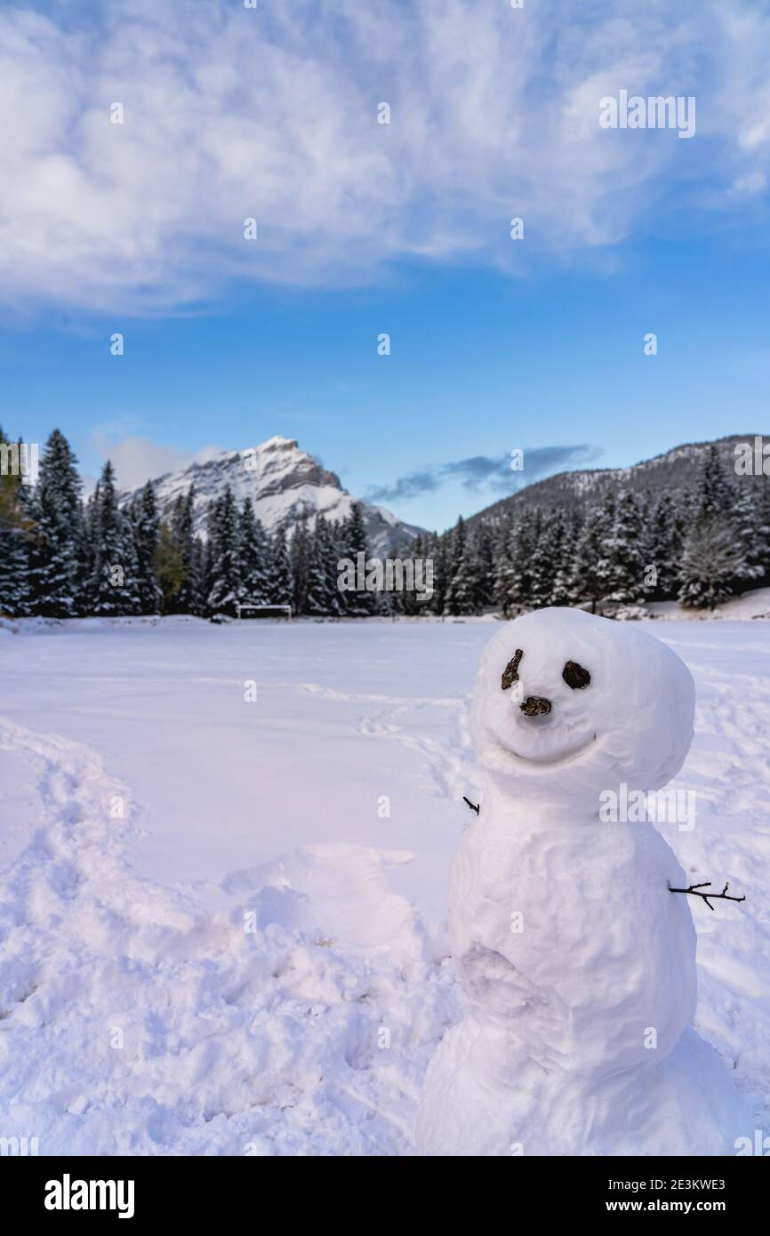 Un bonhomme de neige souriant dans l'aire de jeux enneigée. Cascade Mountain et arbres en arrière-plan. Parc national Banff, Rocheuses canadiennes. Banque D'Images