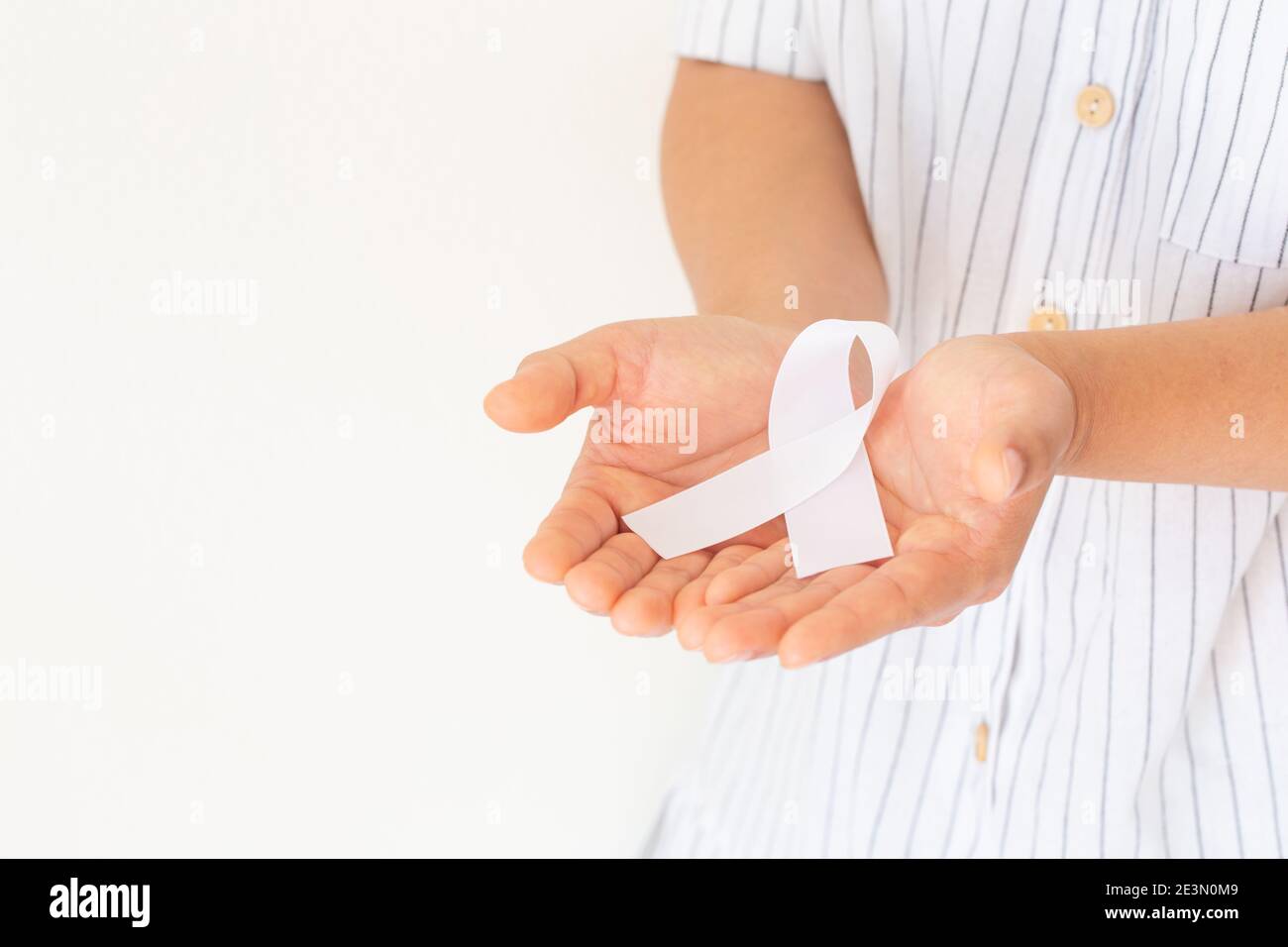 Mains tenant un ruban blanc perle noeud sur fond blanc, espace de copie. Sensibilisation au cancer du poumon, symbole du cancer du Mésothéliome et du rétinoblastome. Signal de pureté Banque D'Images