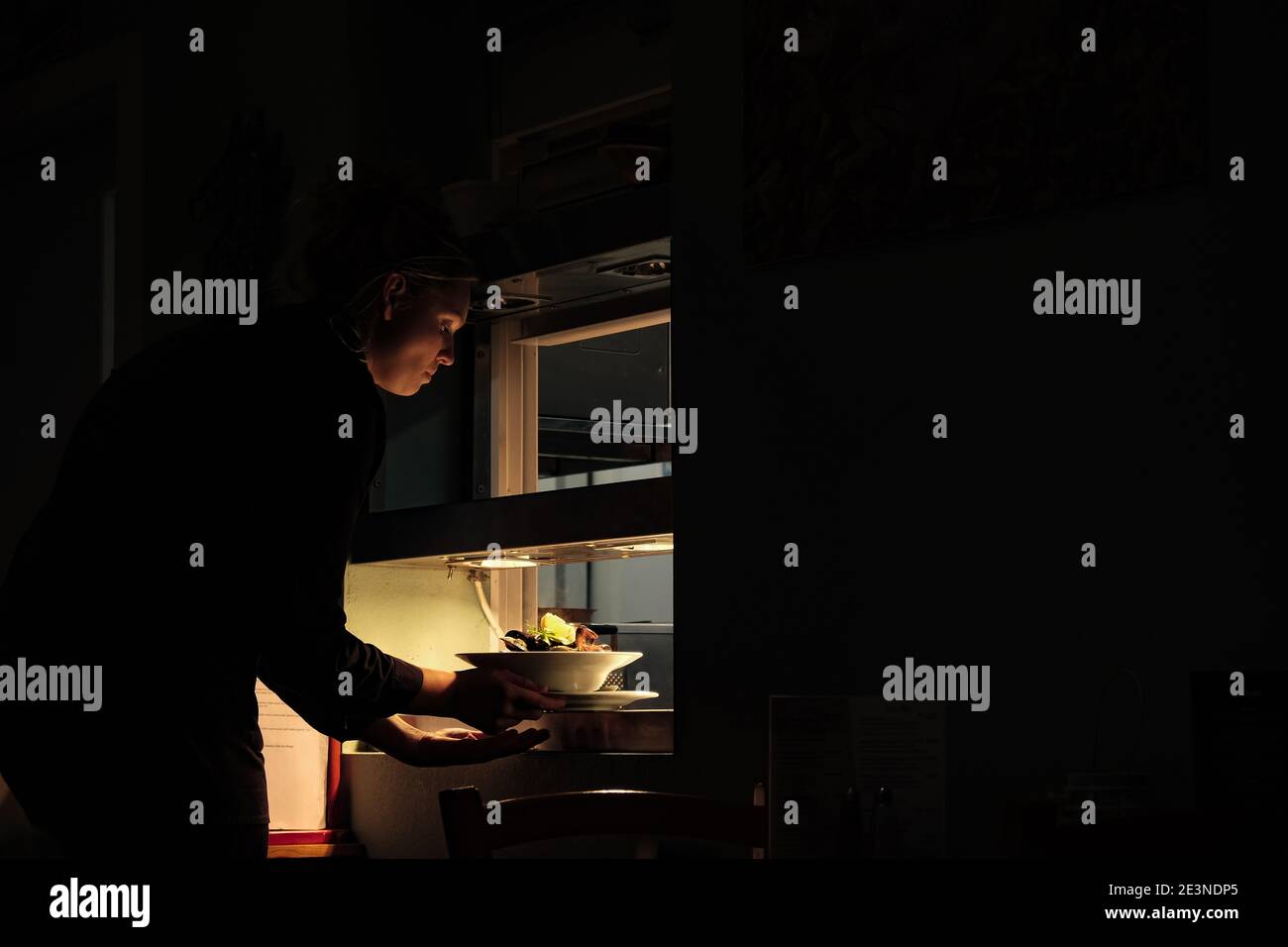 Chiaroscuro image de la serveuse qui prend des aliments à la vapeur dans la fenêtre du service du restaurant, Dingle, Irlande Banque D'Images