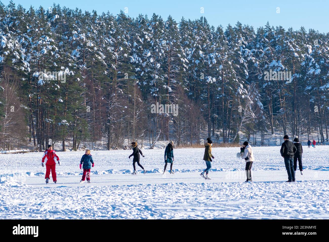 Les gens skier sur un lac gelé avec des arbres de forêt recouvert de neige en arrière-plan Banque D'Images