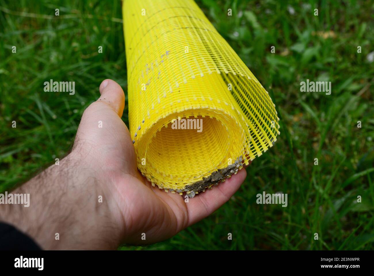 Un homme tient un rouleau de toile de fibre de verre auto-adhésif jaune pour  le plâtrage, le treillis de stuc de fibre de verre pour la façade et la  décoration travaille comme