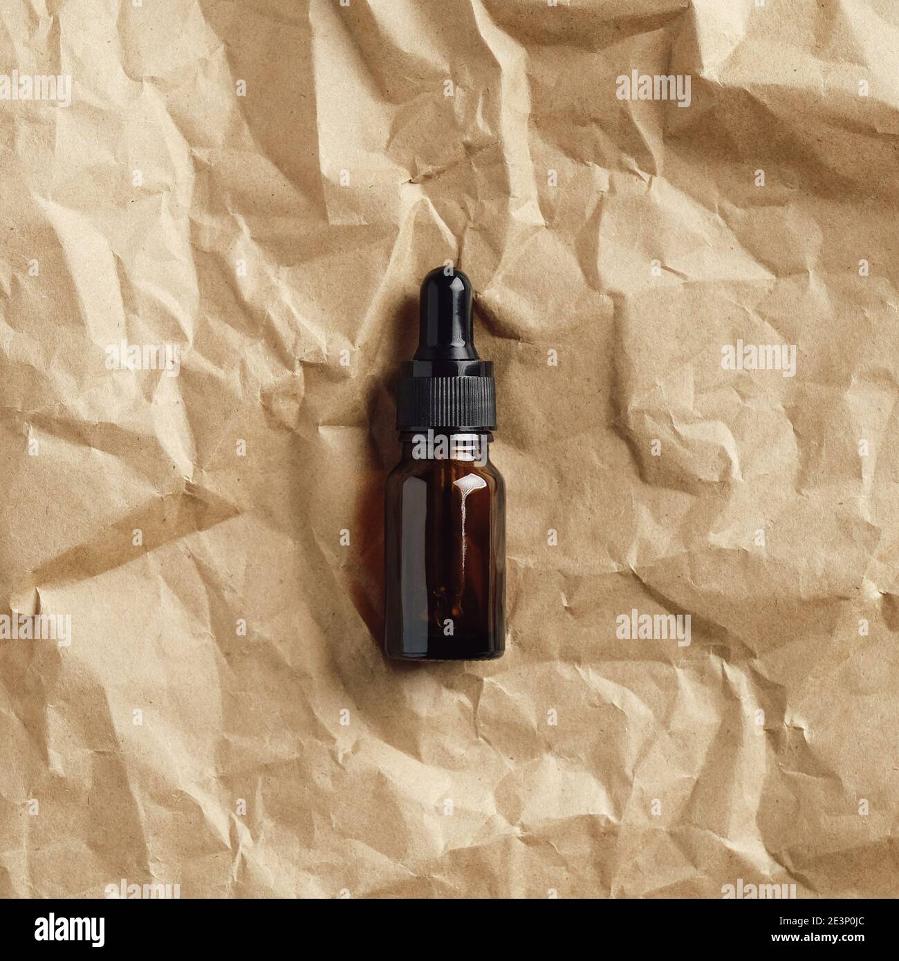Huile aromatique naturelle dans un flacon compte-gouttes en verre ambré sur papier froissé, vue du dessus. Design d'emballage de produits de beauté bio Banque D'Images