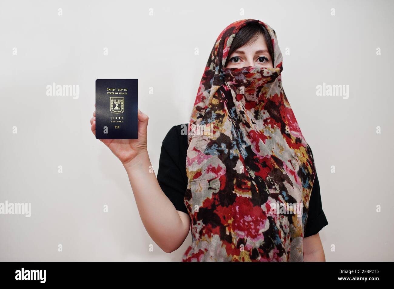 La jeune femme musulmane arabe vêtue de hijab tient le passeport de l'État d'Israël sur fond de mur blanc, portrait de studio. Banque D'Images