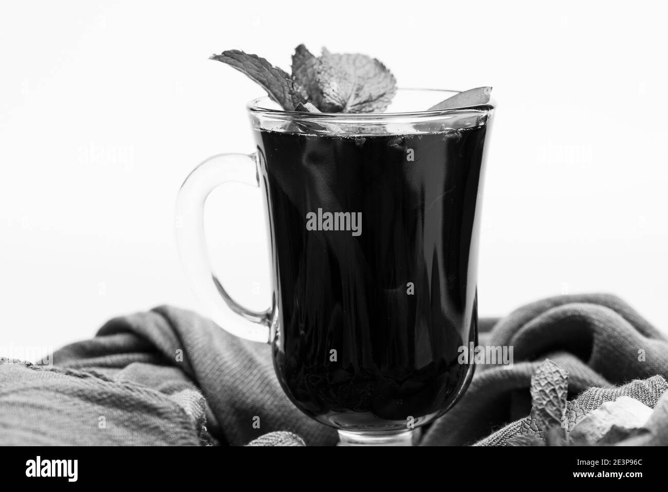 Vin chaud en verre et décor. Concept de bar et de dégustation de vins. Feuilles de menthe, racine de gingembre et tranches de pomme en verre. Verre de vin chaud rouge sur fond blanc et tissu brun. Banque D'Images
