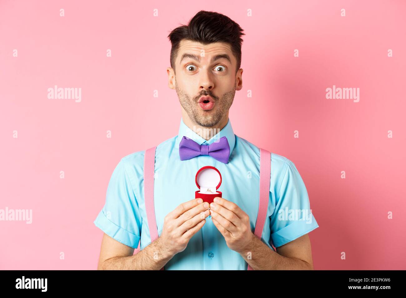 Saint-Valentin. Homme drôle avec moustache et noeud-cravate, regardant  excitée et montrant l'anneau d'engagement, demandant à la petite amie de  l'épouser, debout sur rose Photo Stock - Alamy