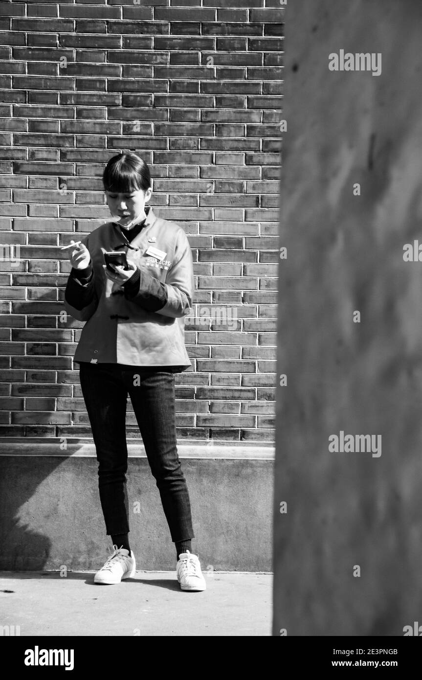 Une employée de Swatch utilise son téléphone tout en fumant lors d’une pause dans le quartier branché de Xintiandi à Shanghai. Banque D'Images