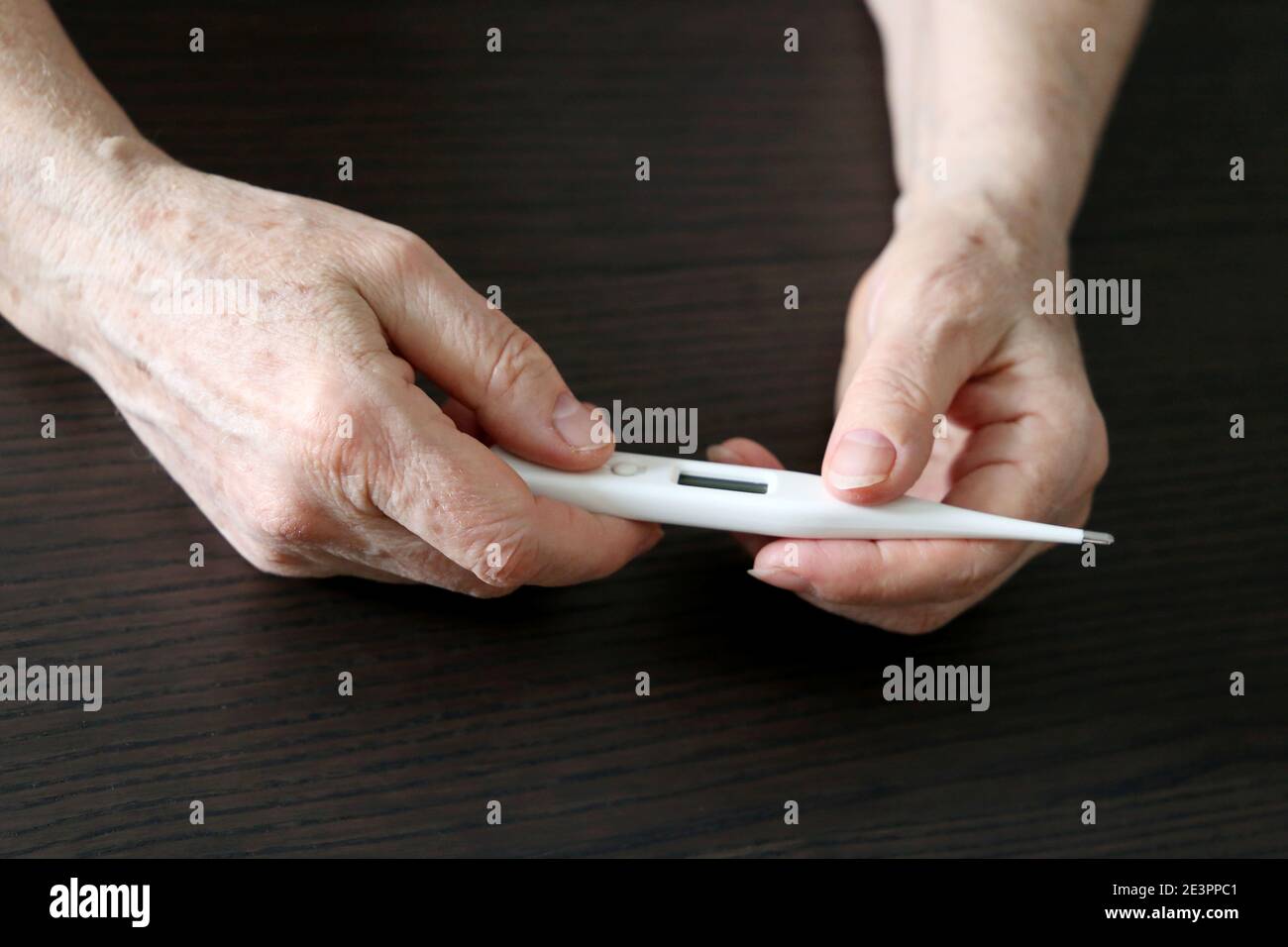 Femme âgée mesurant la température corporelle, concept de fièvre, symptômes du coronavirus. Thermomètre numérique dans les mains femelles froissées Banque D'Images
