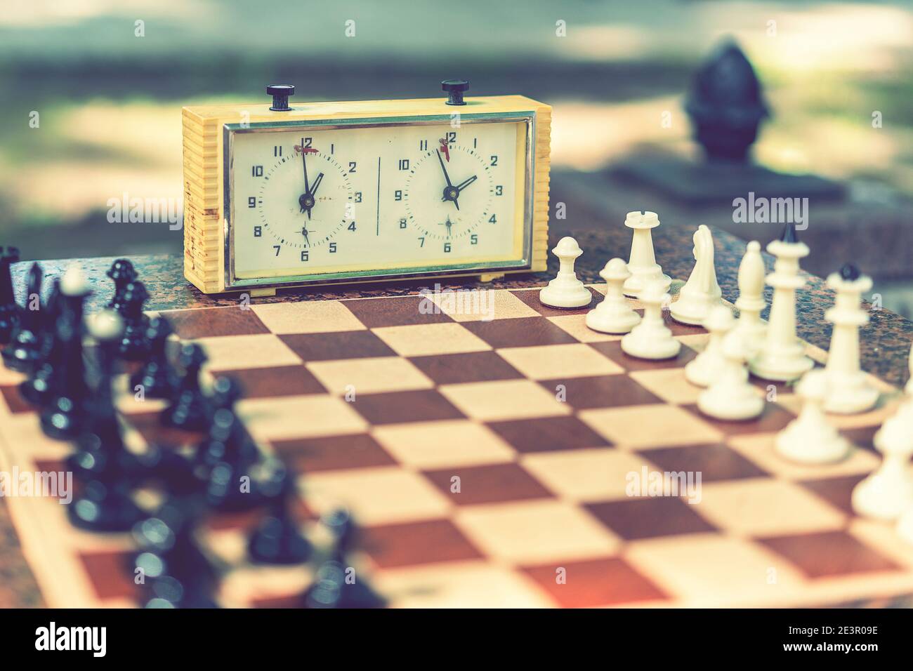 Échiquier avec pièces et horloge sur un bureau en bois en relation avec le tournoi d'échecs. Pièces d'échecs et chronomètre sur une planche dans le parc. Ton Banque D'Images