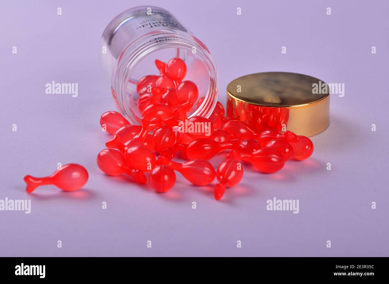 Capsules pharmaceutiques de gélatine rouge tendre sur fond violet. Capsule polypeptidique Caviar essence liquide dilue les lignes fines éclaircissement Banque D'Images