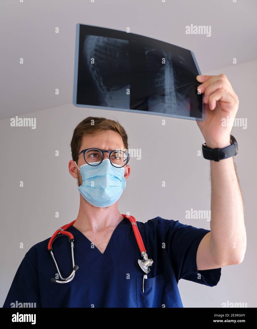 un beau médecin hommes portant un gommage, un stéthoscope et un masque facial regardant une radiographie pendant la pandémie de cov 2 du sras covid 19 Banque D'Images