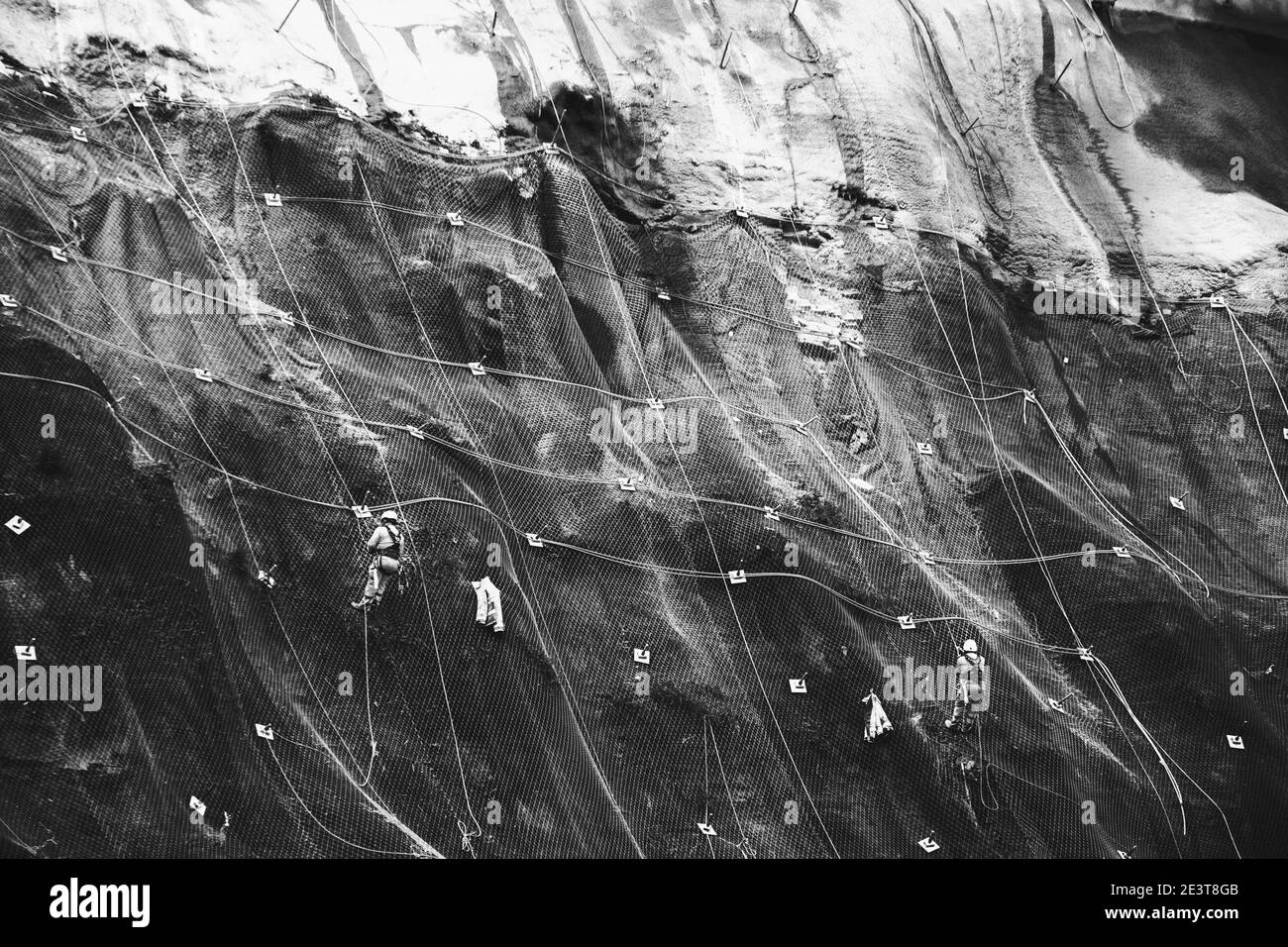 Les travailleurs renforcent la pente de la montagne avec un maillage métallique empêchant la chute sur la route.Hondarribia, Espagne.Photo historique noir blanc. Banque D'Images