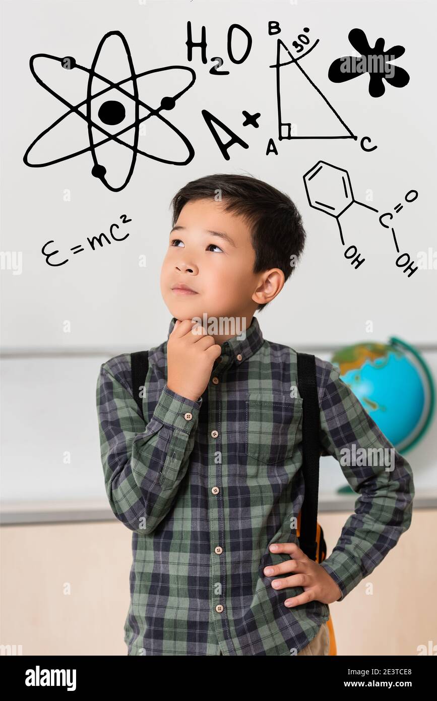 Lycéen asiatique attentionné avec main sur la hanche dans la salle de classe avec illustration de l'école Banque D'Images