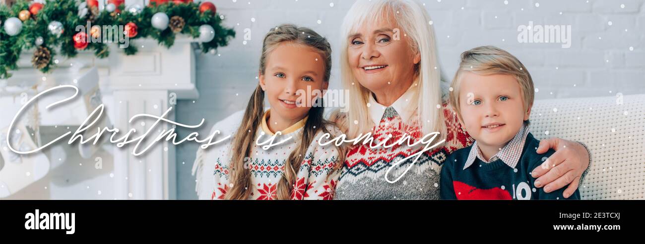 Une grande-mère heureuse embrassant des petits-enfants assis sur un canapé ensemble, Noël est à venir illustration, bannière Banque D'Images