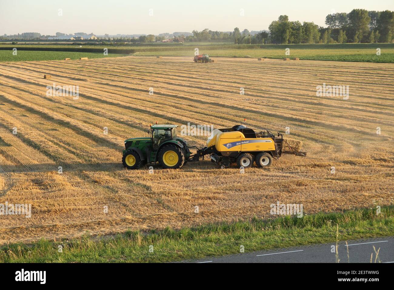 vue aérienne sur un champ où se trouvent les tracteurs avec presses à balles fabrication de balles de paille dans la campagne hollandaise de zeeland à une chaude soirée d'été Banque D'Images