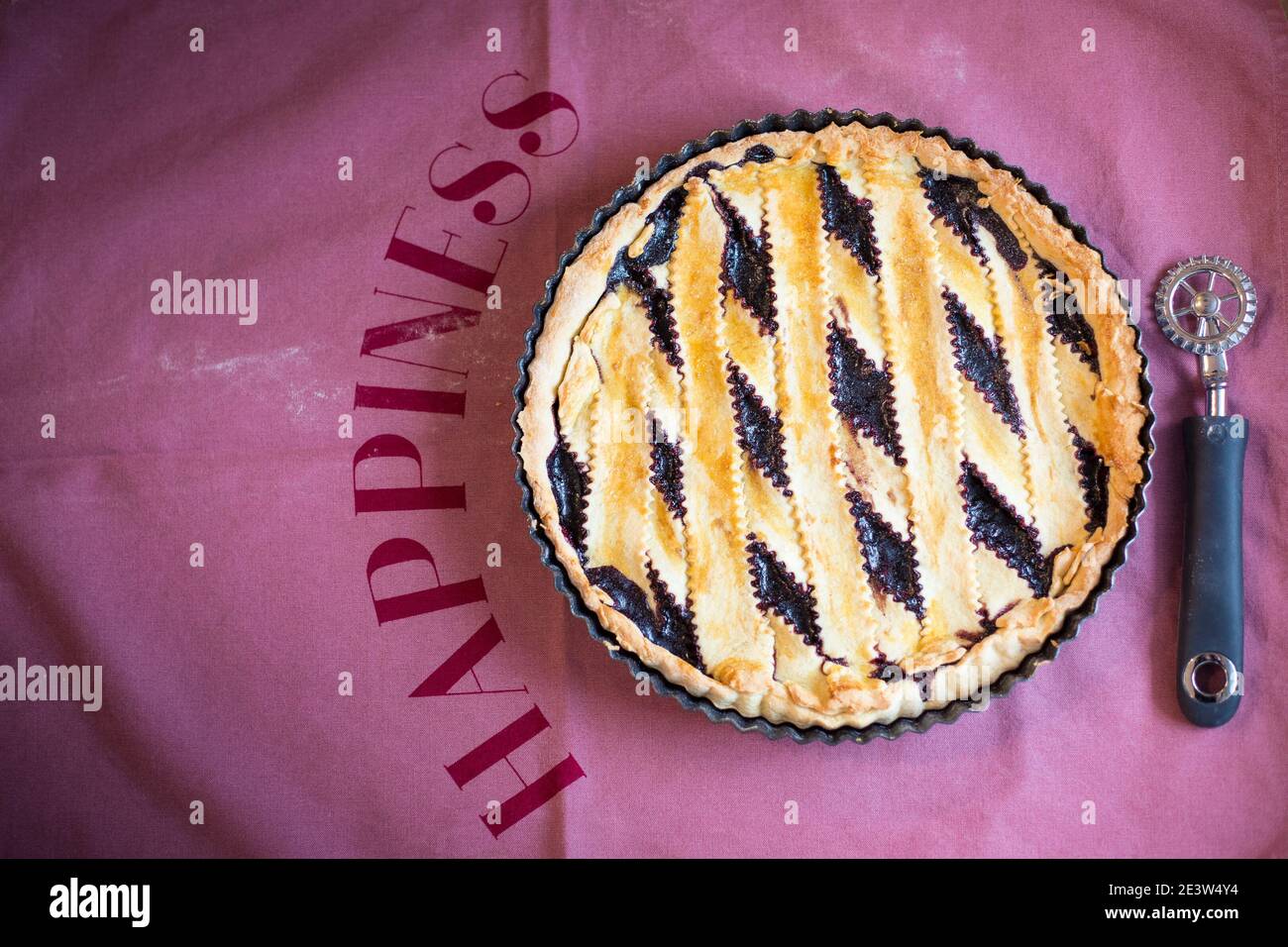 Tarte à la confiture faite maison sur un chiffon rose avec le mot « bonheur », et une roue de couteau à pâtisserie. Vue de dessus, plat, idée de dessert de Saint-Valentin ou fond avec cop Banque D'Images