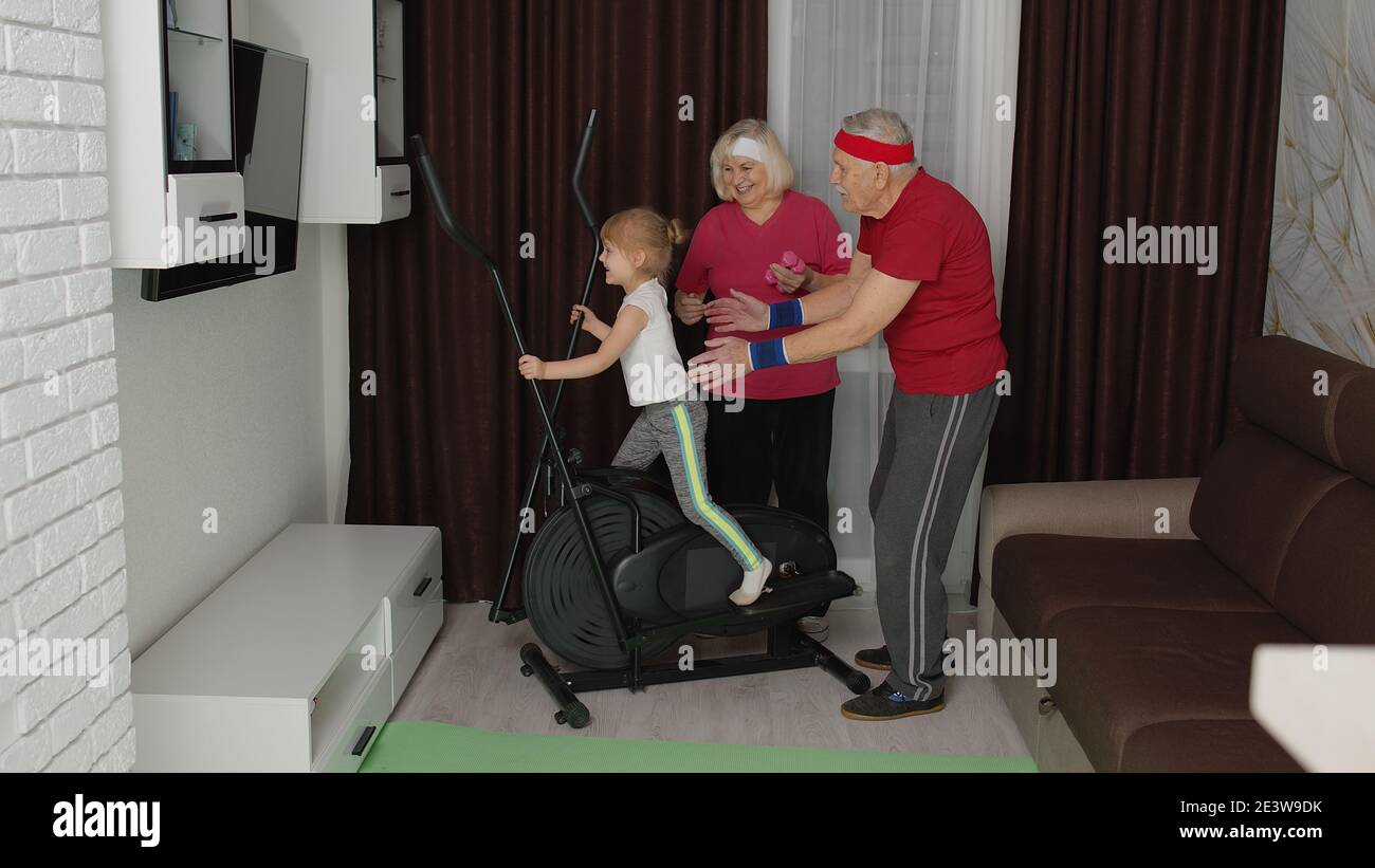 Grand-père mature senior actif, grand-mère entraînement enfant petite-fille comment utiliser des exercices cardio-vasculaires Orbitrek dans la salle de séjour à la maison. Sport d'entraînement pour les jeunes enfants. Coache homme et femme Banque D'Images