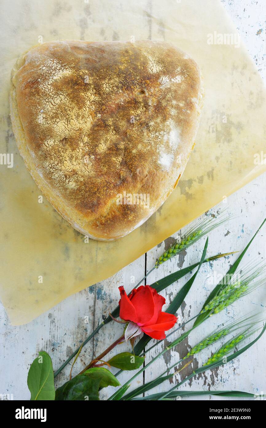 Rose rouge, épis de blé vert frais et pain en forme de coeur sur table rustique Banque D'Images