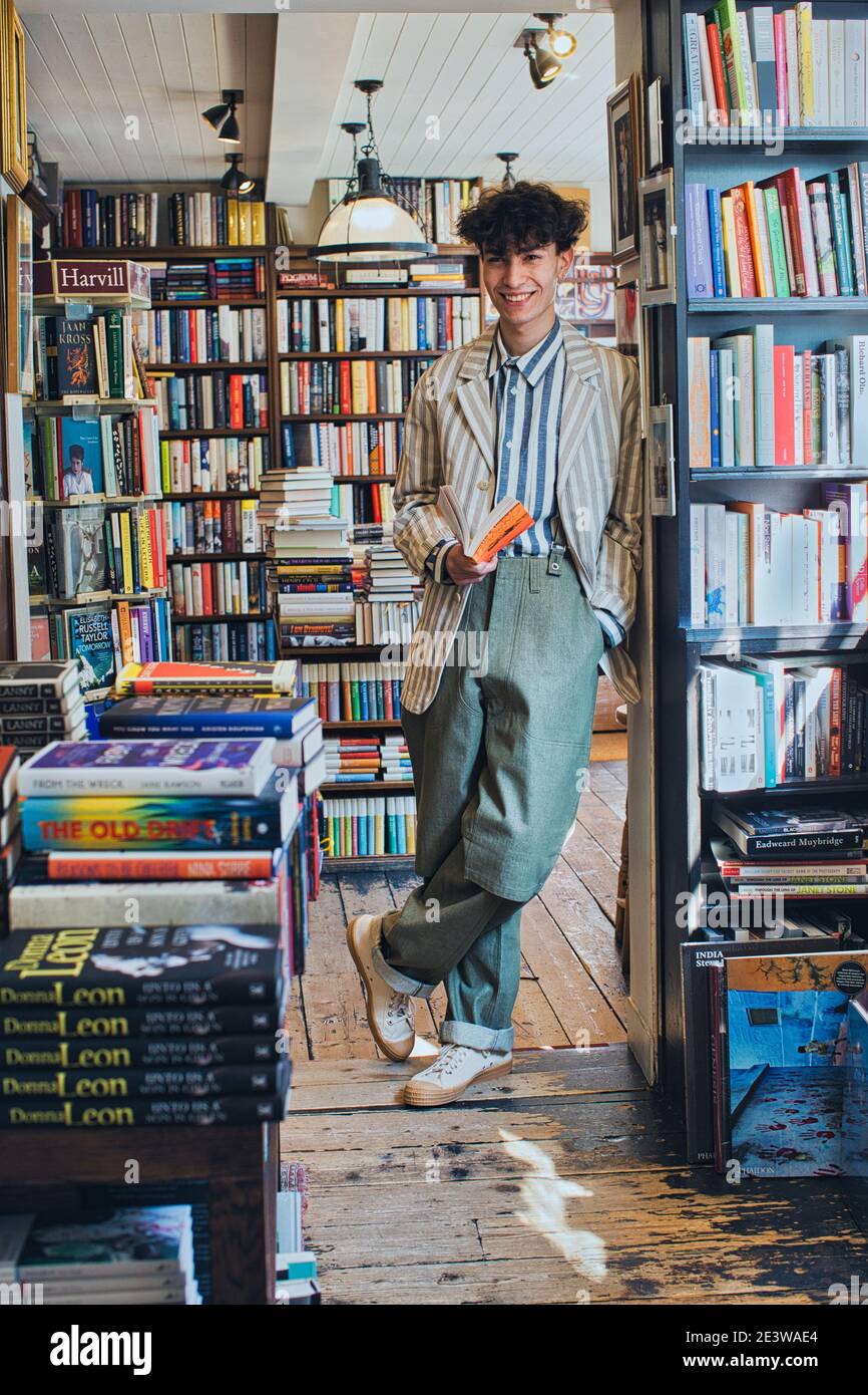 jeune homme souriant tenant un livre dans une librairie Banque D'Images