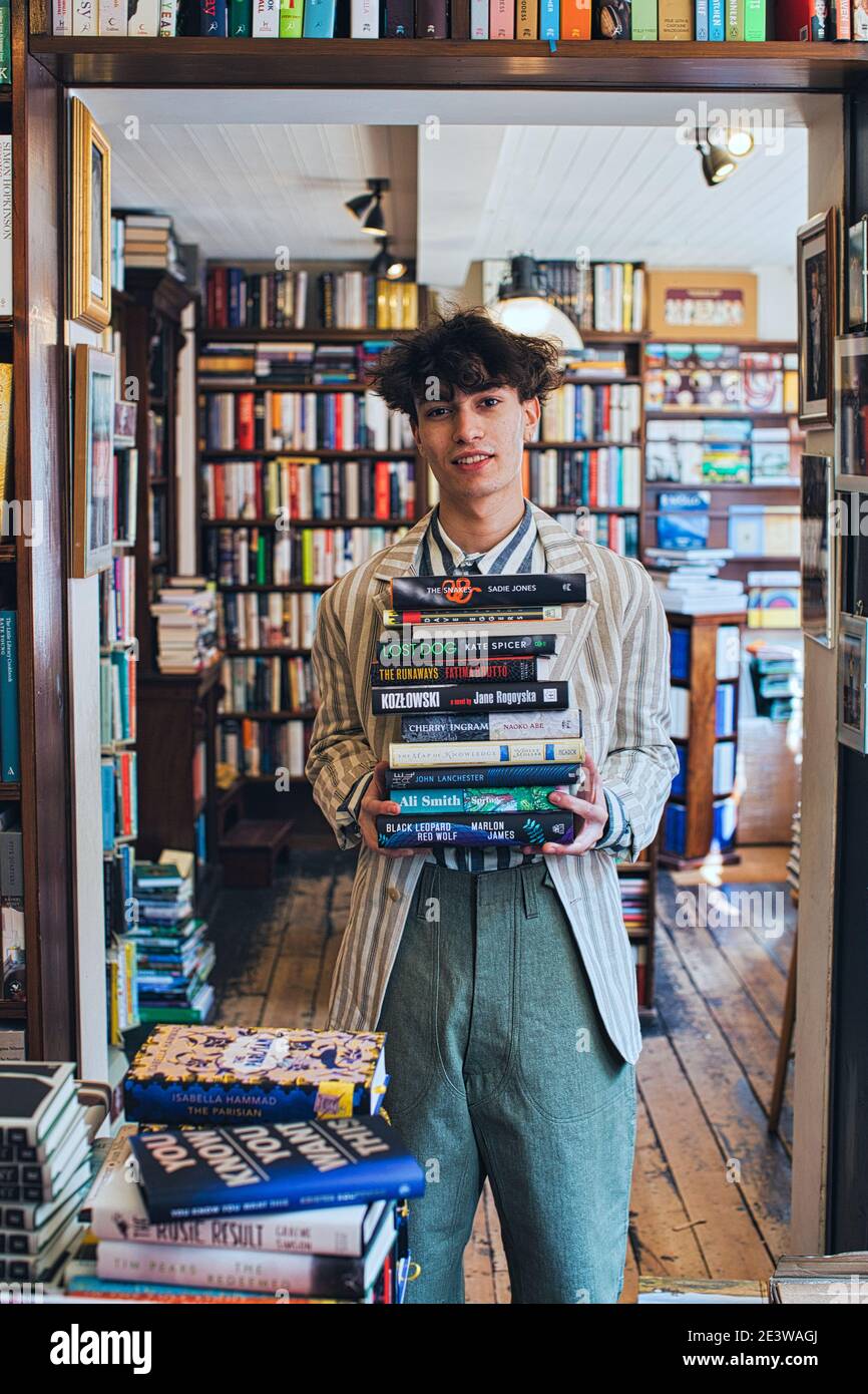 jeune homme tenant une pile de livres dans la librairie Banque D'Images