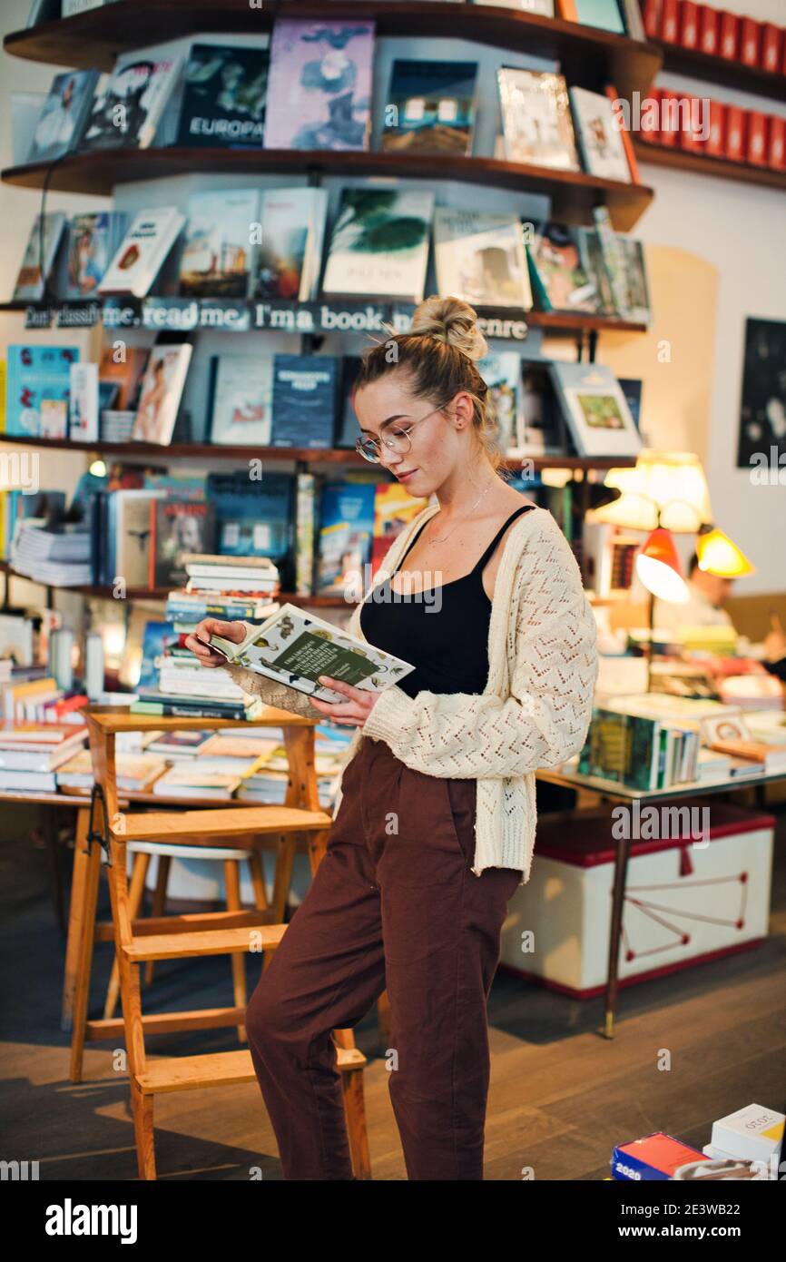 Jeune femme avec lunettes lecture Livre dans la librairie Banque D'Images