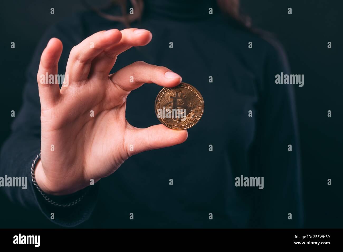 Les mains des femmes tiennent une pièce de monnaie en bitcoin sur fond noir. Banque D'Images