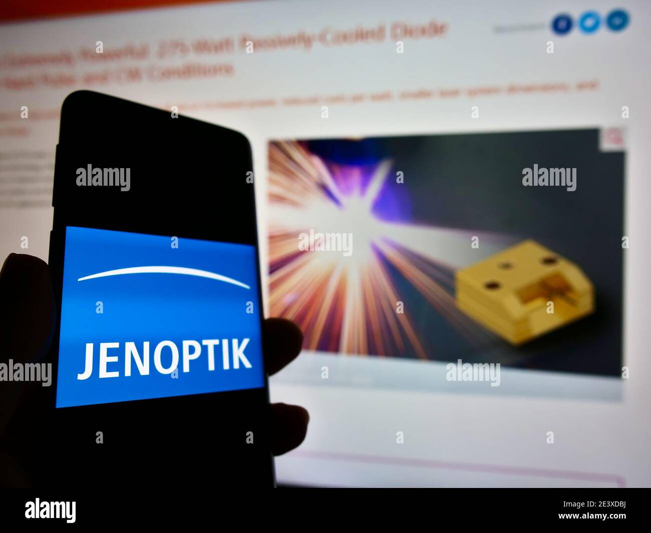 Personne tenant un téléphone portable avec le logo de la société allemande de photonique Jenoptik AG affiché en face de la page web. Mise au point sur l'écran du téléphone mobile. Banque D'Images