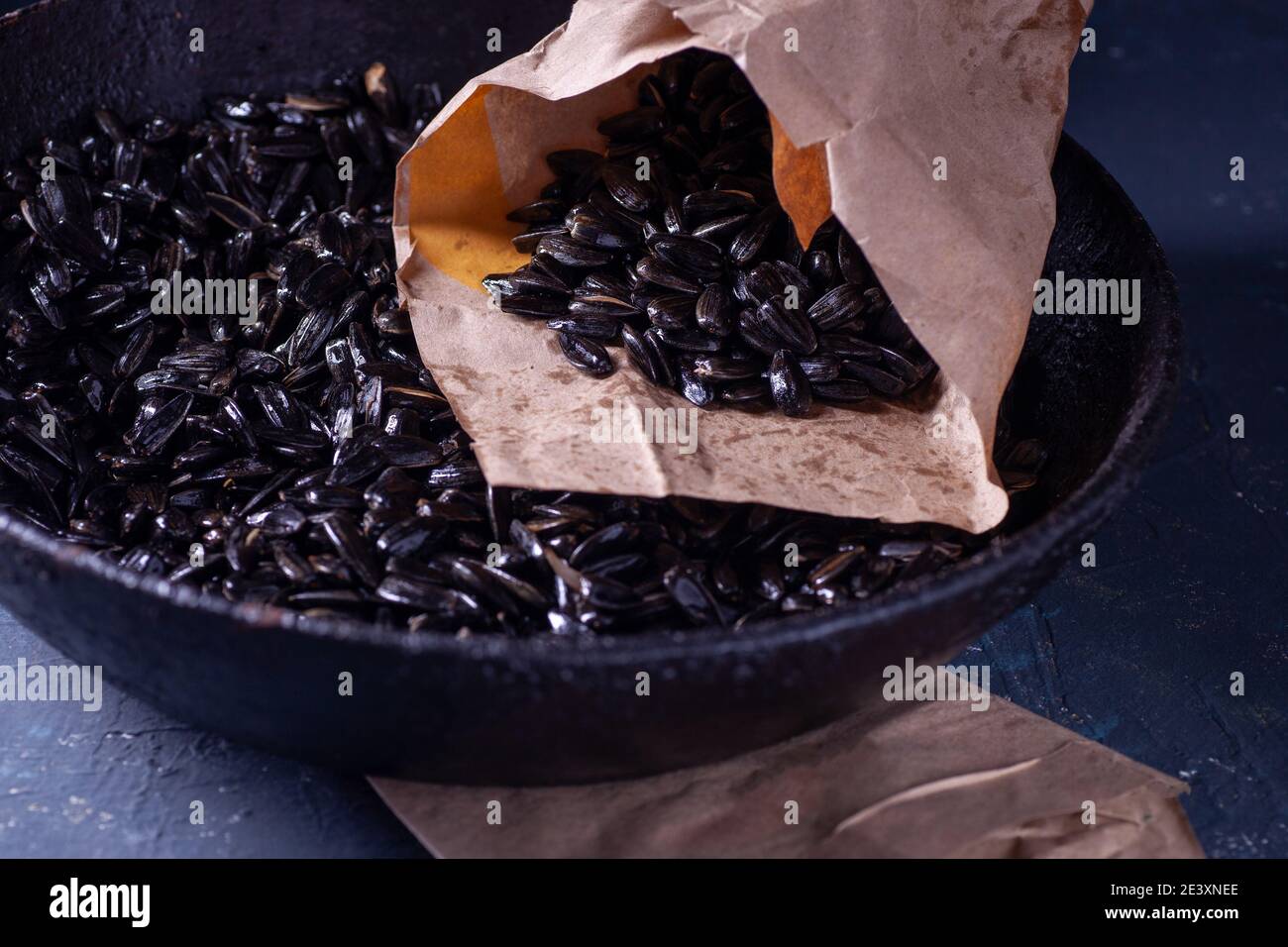 graines de tournesol dans un sac de papier et dans une poêle en fonte noire charrée avec une poignée sur une table en béton gris dans une clé sombre, rustique Banque D'Images