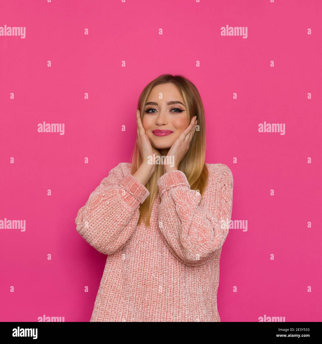 Bonne mignonne femme blonde dans un chandail rose tient la tête dans les mains. Taille haute studio tourné sur fond rose. Banque D'Images