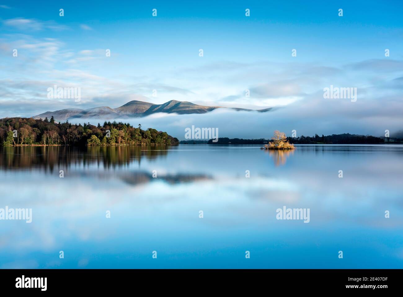 Ciel bleu, lumière du soleil dorée sur une petite île et inversion de nuages sous Skiddaw. Tout se reflète dans un Derwentwater calme, Lake District, Angleterre. Banque D'Images