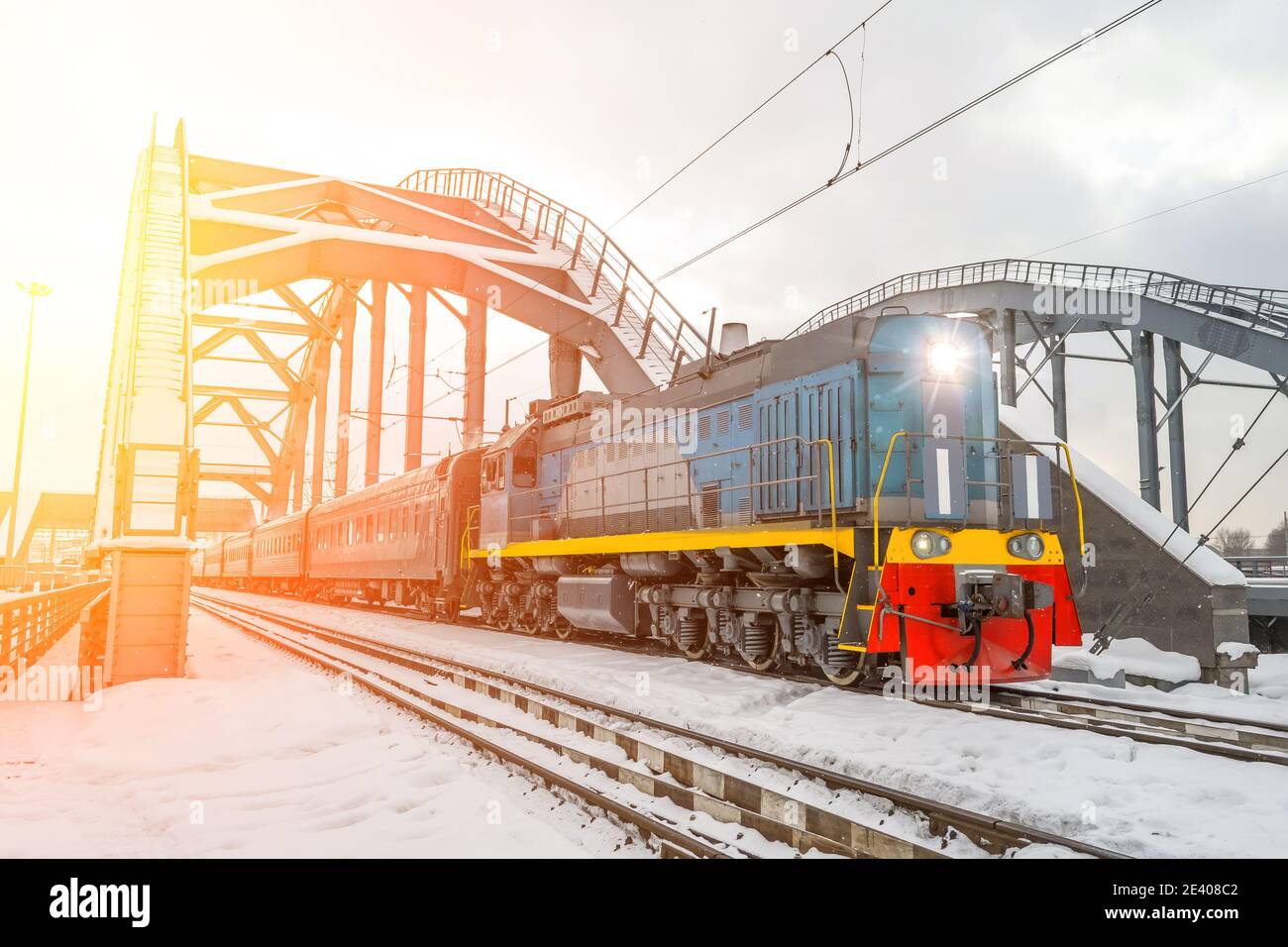 La locomotive à moteur diesel dépasse les voitures de tourisme par le pont ferroviaire dans la neige d'hiver Banque D'Images