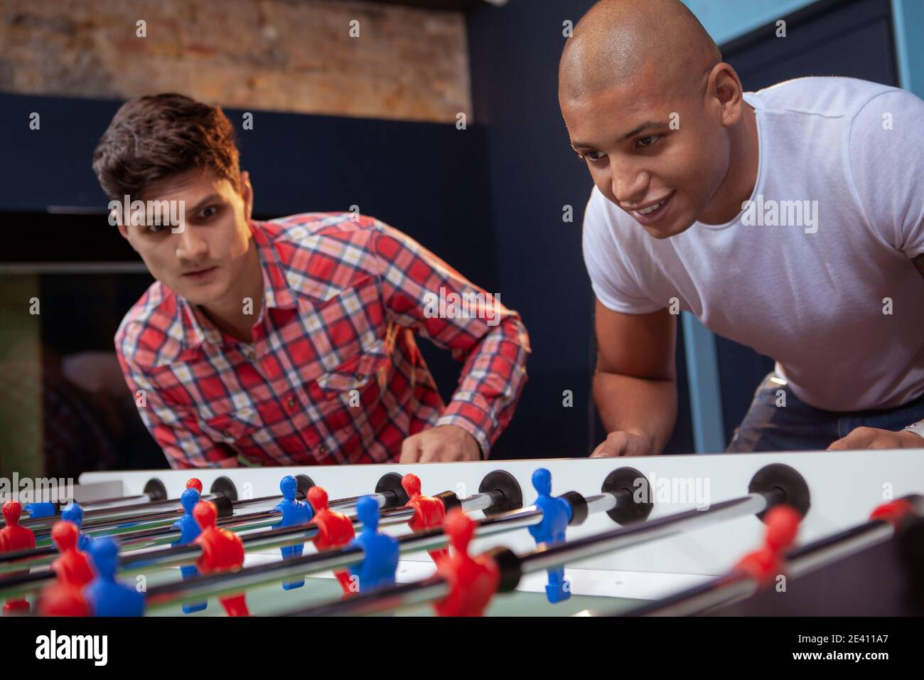 Deux jeunes amis masculins jouant au baby-foot. Beau homme africain appréciant jouer au football de table avec son ami Banque D'Images