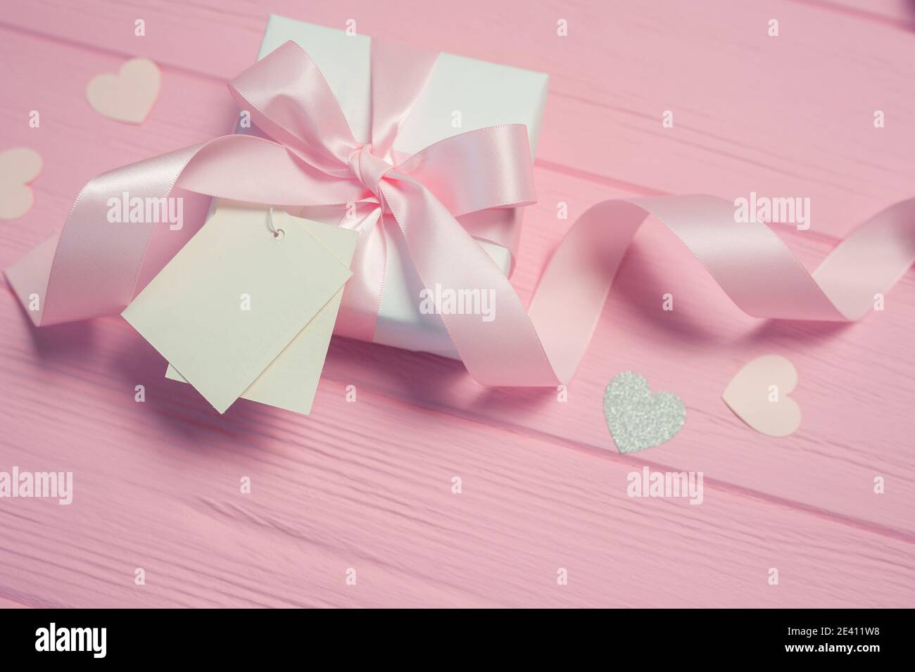 Boîte cadeau blanche avec noeud en satin rose et ruban sur fond de bois rose. L'étiquette de maquette de mariage est incluse pour votre texte. Peut être utilisé pour la Saint-Valentin Banque D'Images