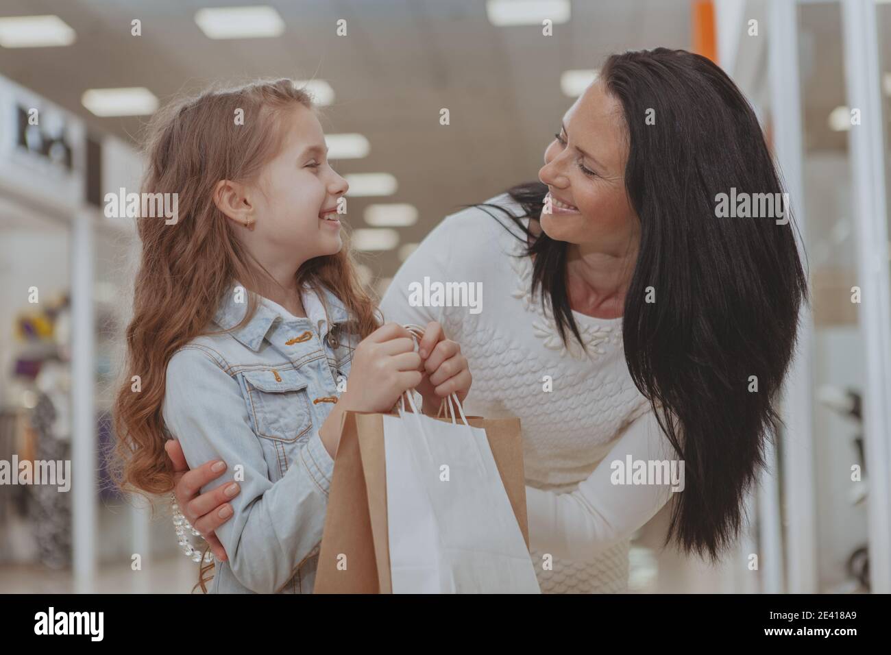 Bonne mère et fille souriant l'une à l'autre, en appréciant le shopping au centre commercial. Belle femme mûre embrassant sa fille, tout en faisant du shopping Banque D'Images