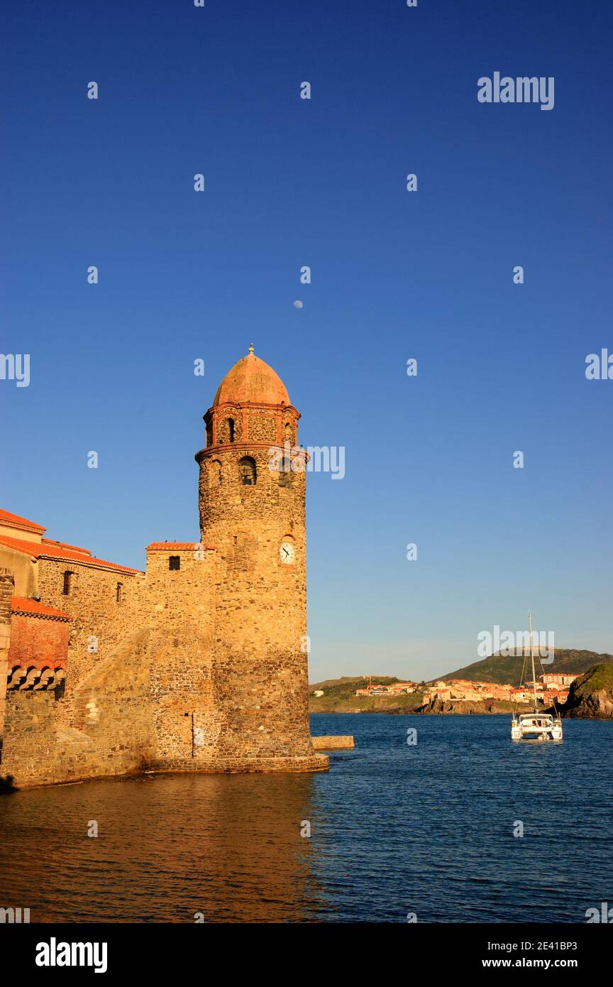 L'église notre-Dame des Anges dans le port de Collioure (France), la lune dans le ciel et le voilier blanc. Coucher de soleil. Banque D'Images