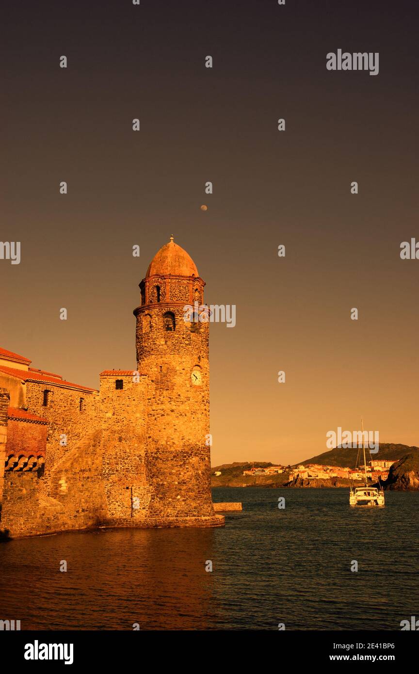L'église notre-Dame des Anges dans le port de Collioure (France), la lune dans le ciel et le voilier blanc. Coucher de soleil. Rétro Banque D'Images