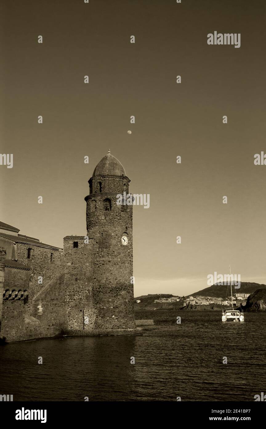 L'église notre-Dame des Anges dans le port de Collioure (France), la lune dans le ciel et le voilier blanc. Coucher de soleil. Photo historique noir blanc. Banque D'Images