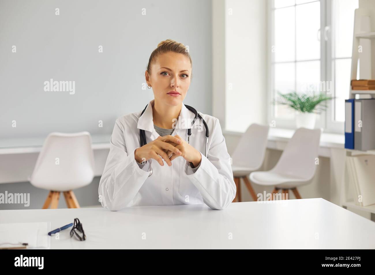 Médecin sérieux assis au bureau et regardant la caméra comme si elle écoute sa patiente Banque D'Images
