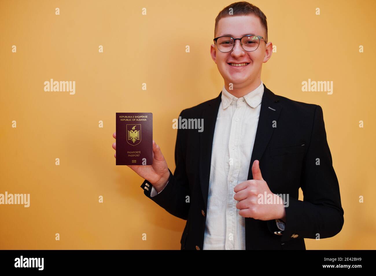 Jeune homme beau tenant la République d'Albanie passeport ID sur fond jaune, heureux et montrer le pouce vers le haut. Concept pays Voyage en Europe. Banque D'Images