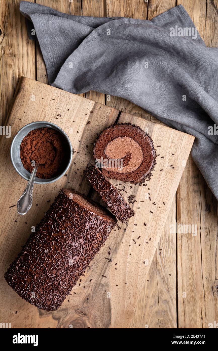 Roulé au chocolat avec garniture au cacao, recouvert de glaçage à la ganache et parsemé de copeaux sur fond de bois Banque D'Images