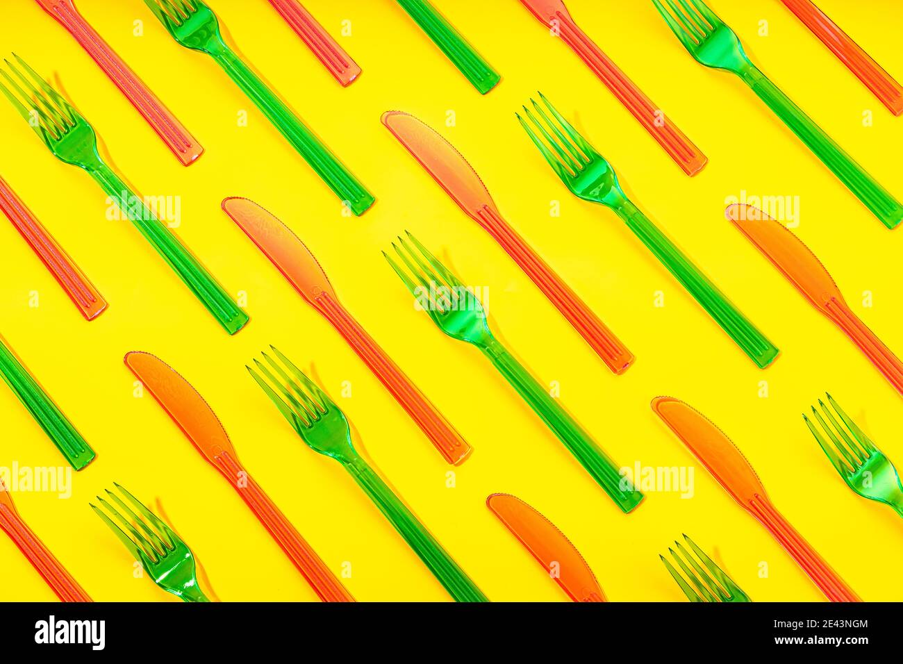 Vue de dessus cadre complet de fourchettes en plastique jetables colorées et couteaux disposés dans l'ordre sur fond jaune Banque D'Images