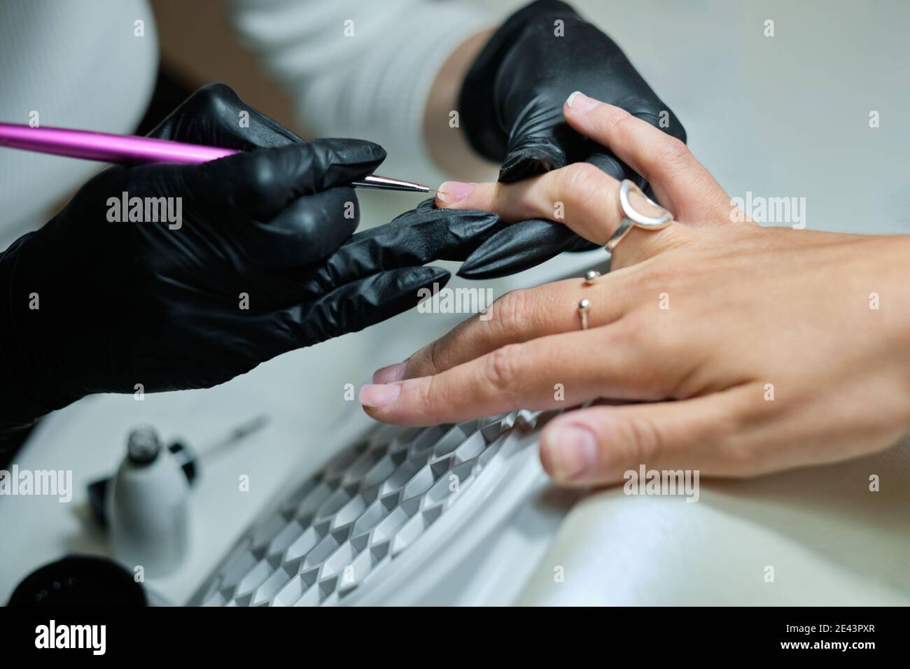 Gros plan de la récolte maître anonyme en gants avec cuticule métallique pousseur tout en faisant la manucure pour femme client dans le salon de beauté Banque D'Images