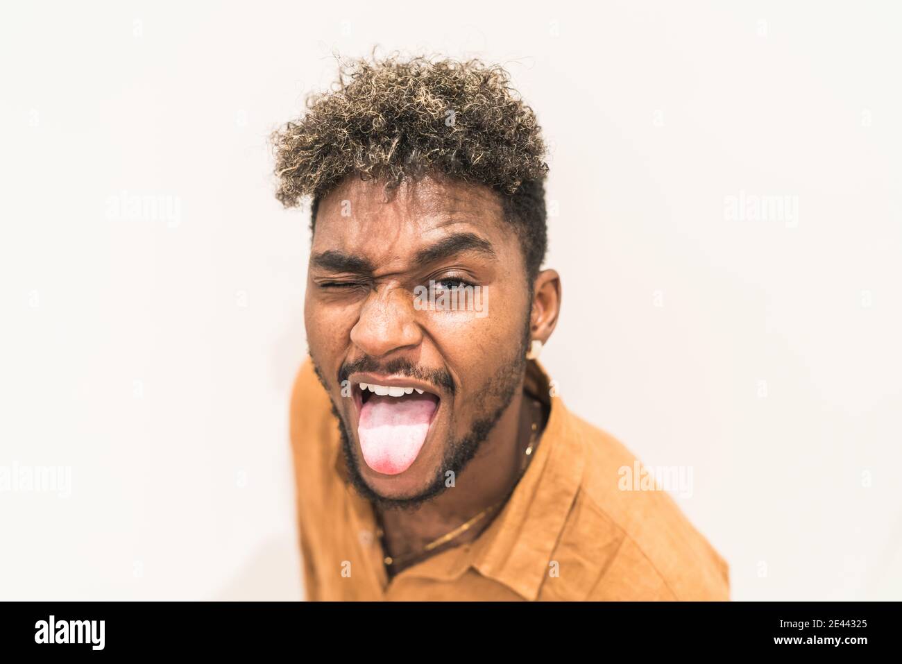 Joli jeune garçon noir de hipster barbu avec des cheveux bouclés et regarder l'appareil photo et sourire en étant assis dans les escaliers à proximité clôture en métal Banque D'Images