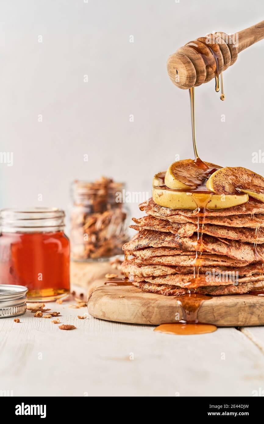 Personne méconnaissable versant du miel du balancier sur une pile de pain croustillant et des tranches de pomme servies sur la table pour le petit déjeuner à la maison Banque D'Images