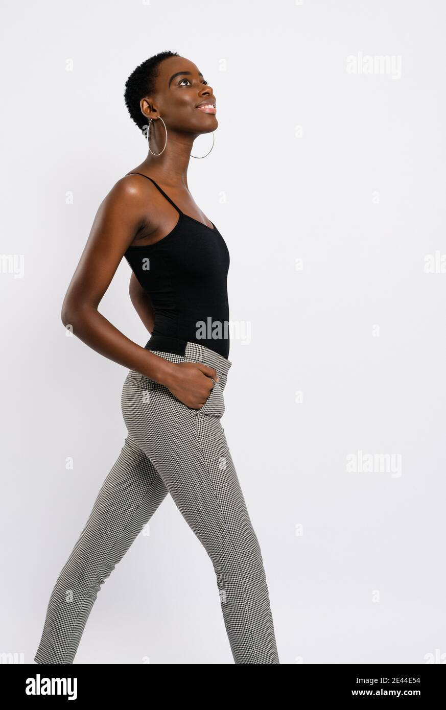 Vue latérale d'une femme afro-américaine mince avec les mains à l'intérieur poches à l'écart sur fond gris Banque D'Images