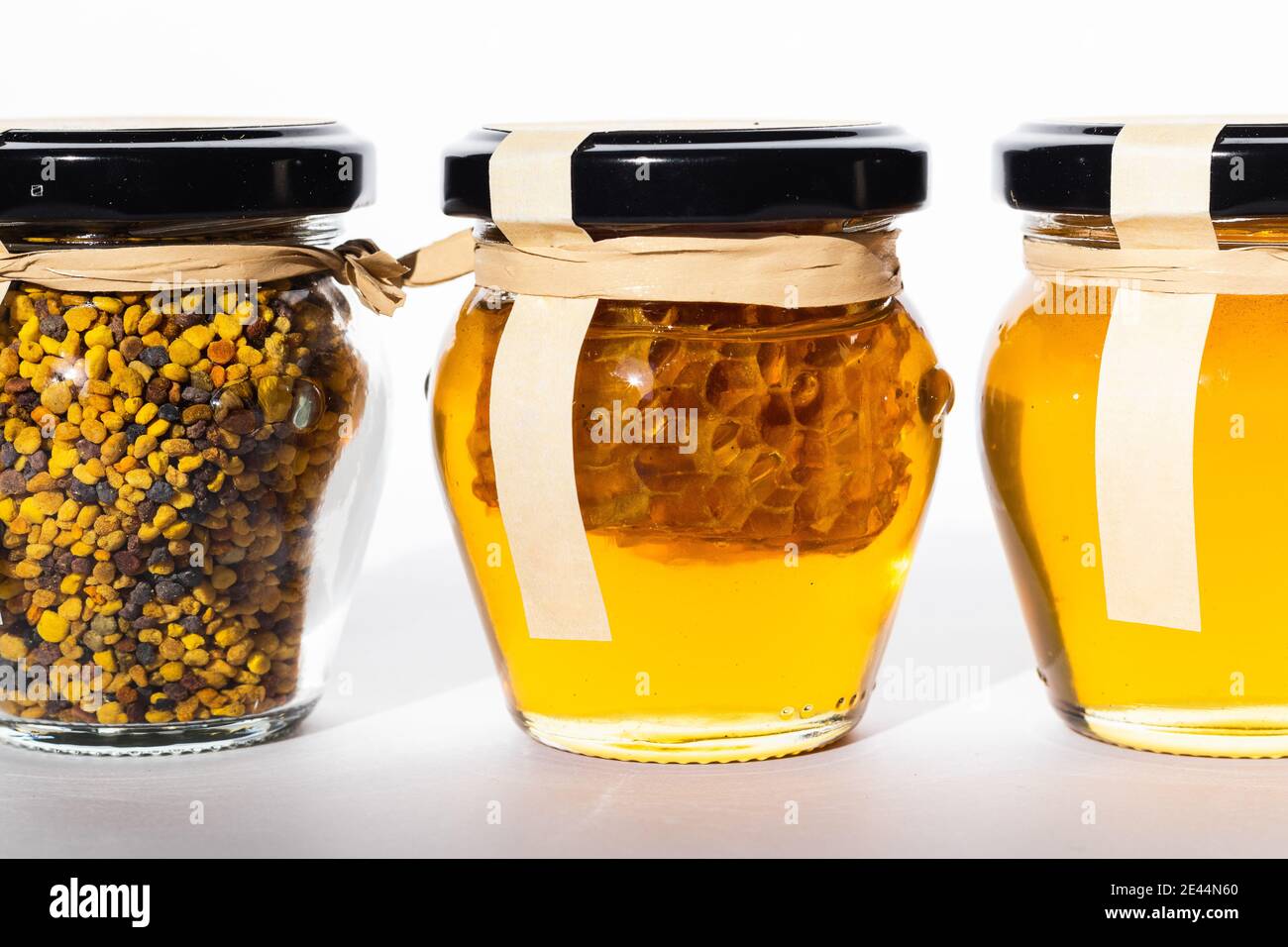 Pots en verre avec du miel frais et du pollen d'abeille placés dans ligne sur la table Banque D'Images