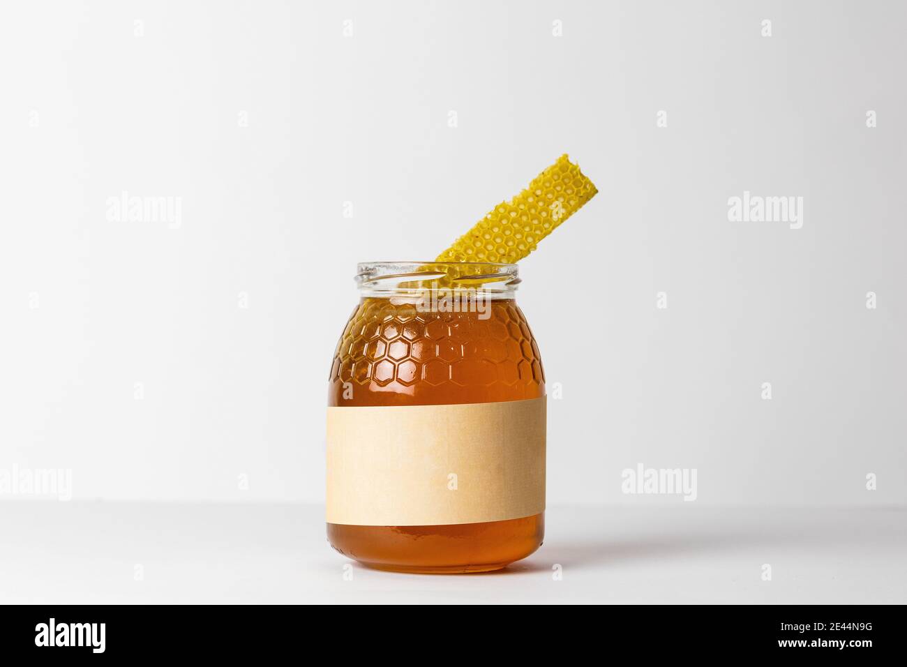 Morceau de nid d'abeille sur le dessus du pot en verre plein de miel doré naturel frais avec fond blanc Banque D'Images