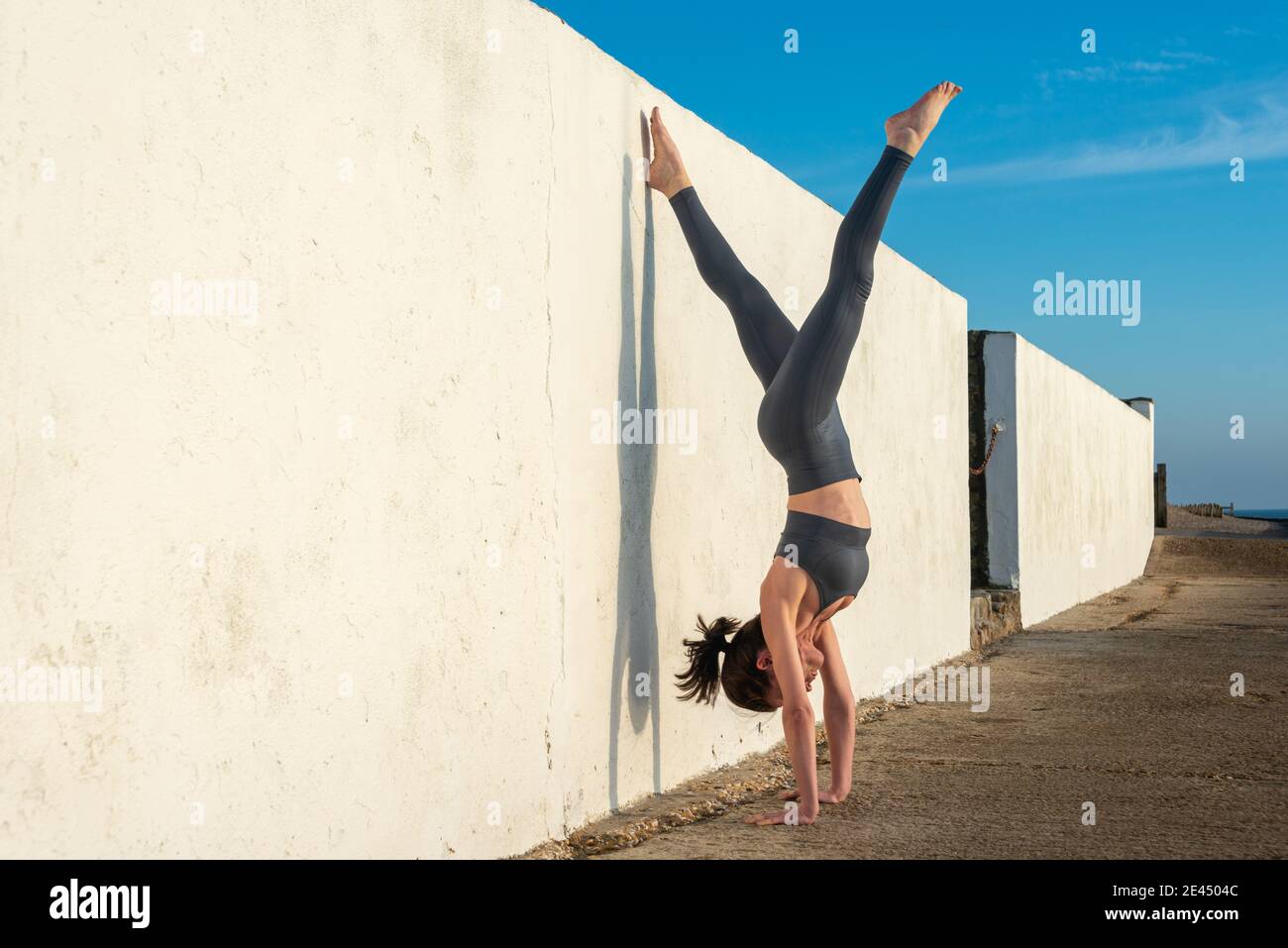 Vue latérale d'une femme flexible penchée au mur et en train de faire yoga avec les jambes étalées le jour ensoleillé Banque D'Images