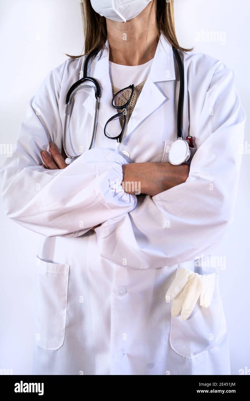 Femelle non reconnaissable, taillée en uniforme blanc et portant un stéthoscope masque médical de protection debout avec les bras croisés Banque D'Images